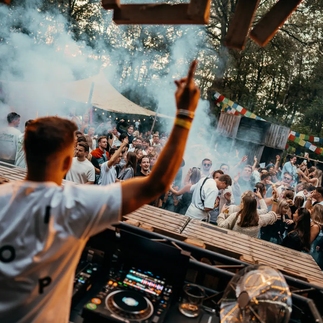 DJ die optreedt op een buitenfestival met een menigte enthousiaste feestgangers die dansen, omringd door bomen.