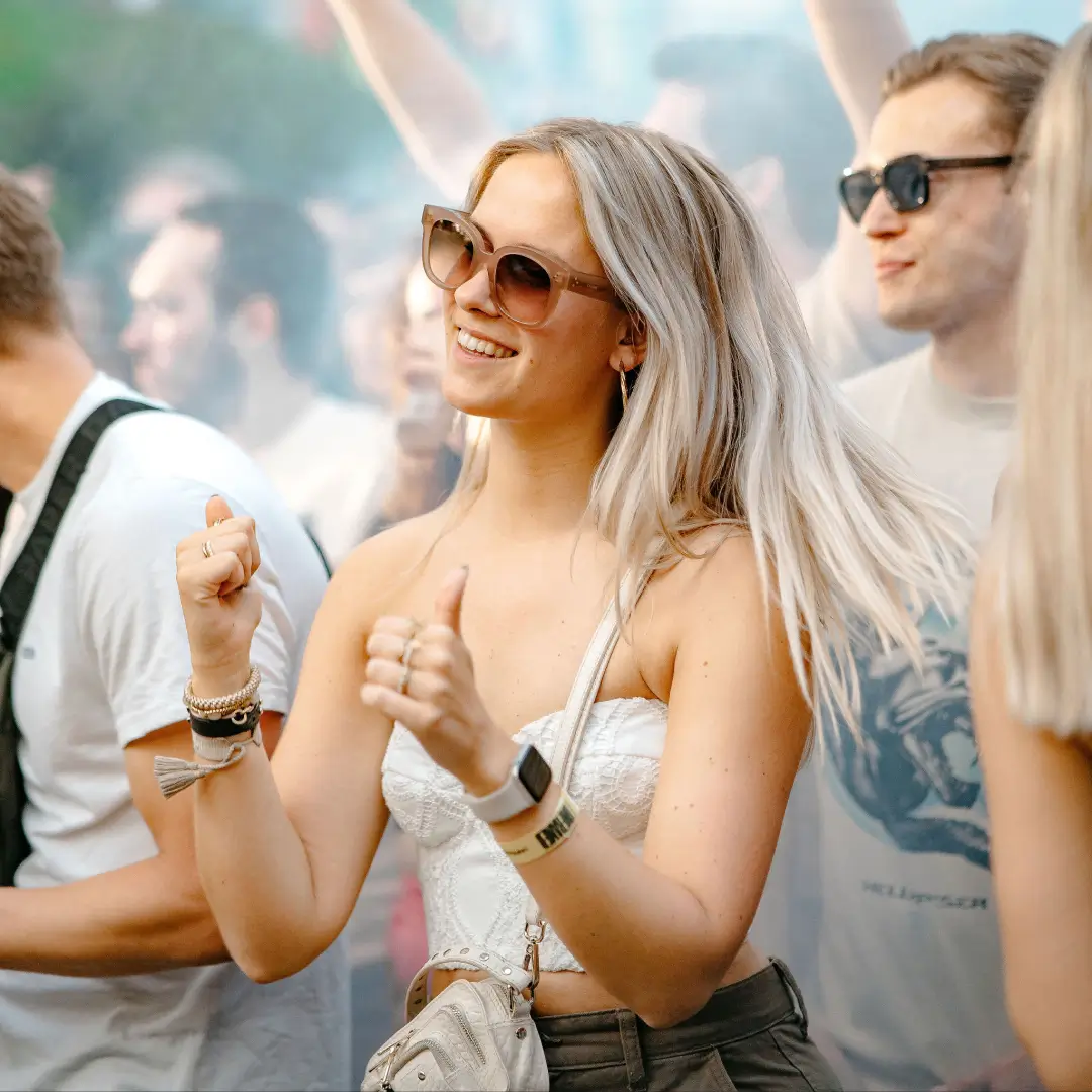 Op het Daycare Festival in Tilburg vangt een vrouw het ritme terwijl ze een wit hemdje en trendy zonnebril draagt.